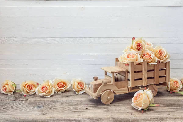 Деревянный игрушечный грузовик с цветами персиковых роз сзади на белом — стоковое фото