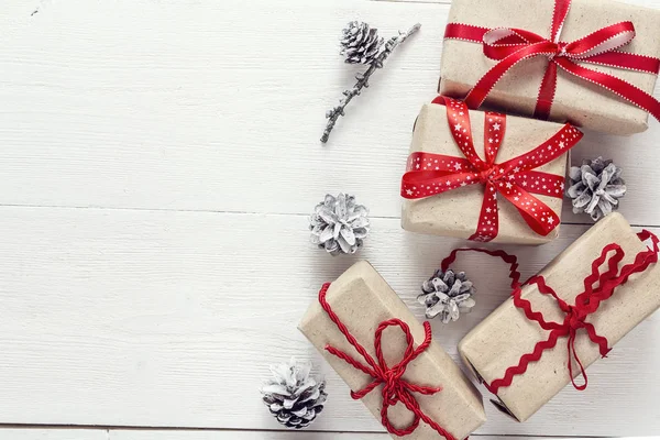 Κουτιά δώρων με κόκκινες κορδέλες και κουκουνάρια σε άσπρο ξύλινες καρτέλα — Φωτογραφία Αρχείου