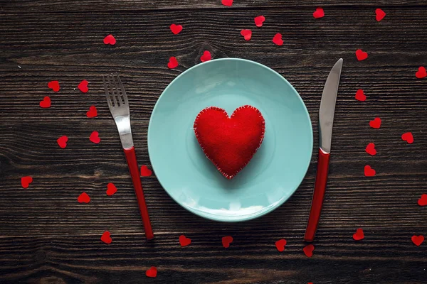 Piatto blu con cuore, forchetta rossa e coltello su un tavolo di legno scuro — Foto Stock