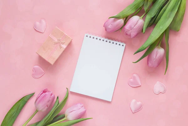 Blocco note aperto bianco con tulipani, confezione regalo e cuori su una ba rosa — Foto Stock