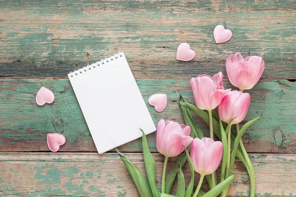 Background with pink tulips, blank notepad  and hearts on blue g — Stock Photo, Image