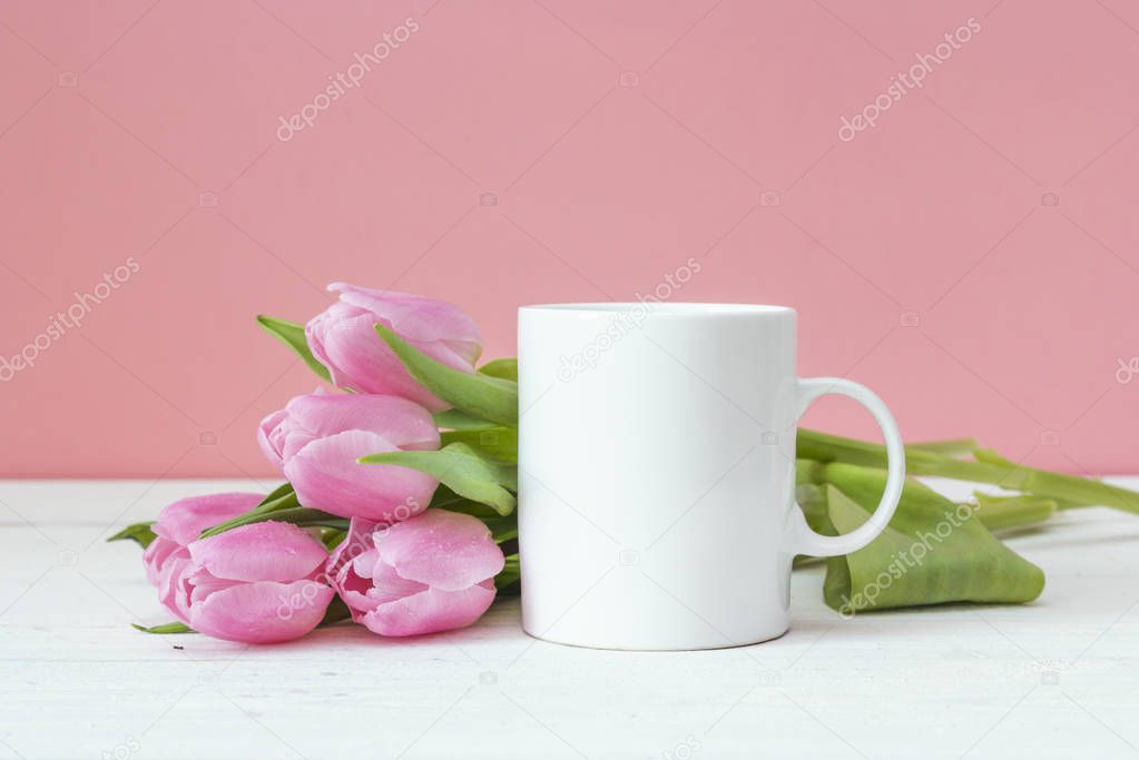 White coffee mug with pink tulips on a pink background. Space fo