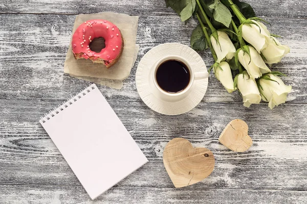 Cuaderno en blanco, taza de café, donut, corazones y rosas blancas en —  Fotos de Stock