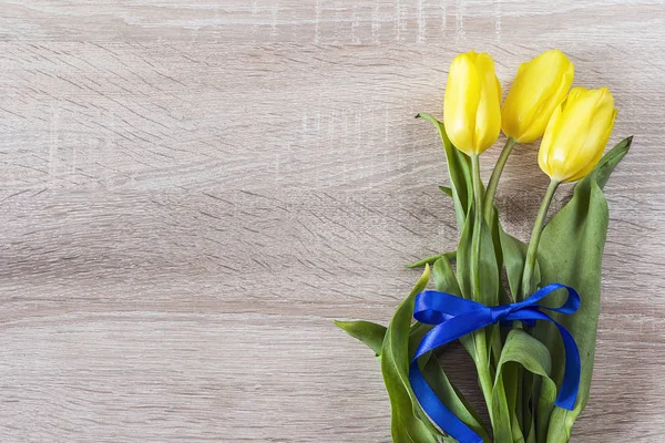 Ramo de tulipanes amarillos con una cinta azul sobre un fondo de madera —  Fotos de Stock