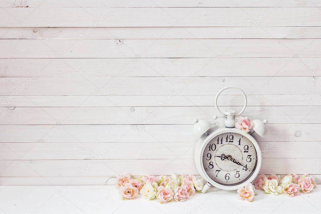 Background with white alarm clock and small pink roses on white 