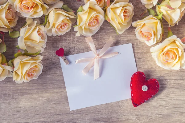 Tarjeta blanca en blanco con una cinta rosa, corazón rojo y rosas melocotón o — Foto de Stock