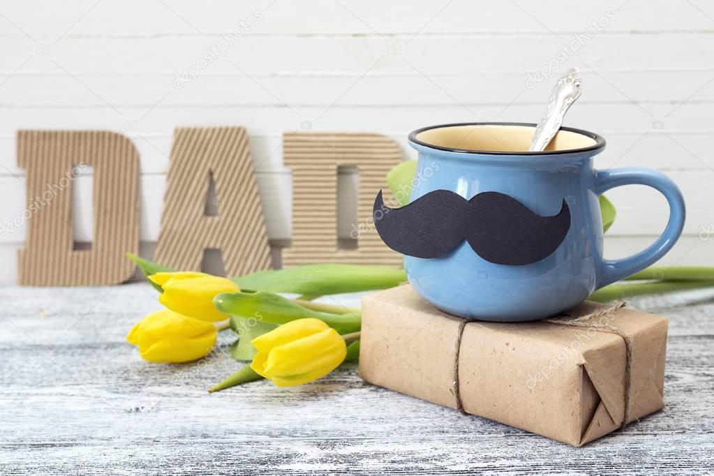 Blue cup with a mustache, gift box, yellow tulips and an inscrip