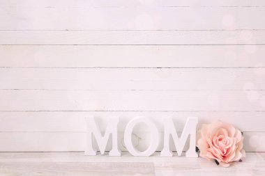 Beyaz ahşap zemin üzerine gül çiçek ile anneler günü mesajı.