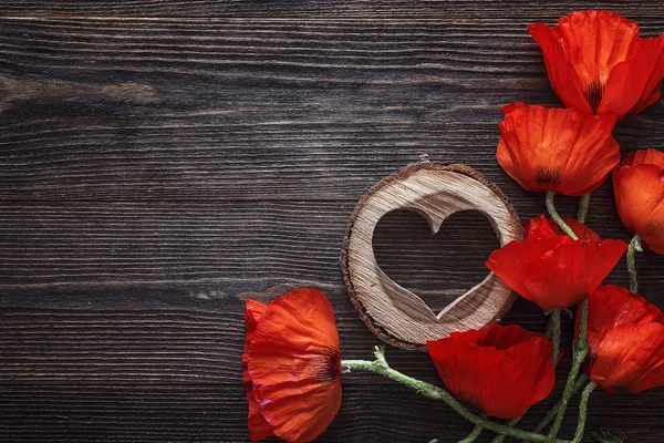 Rode papavers bloemen met houten hart op donkere houten achtergrond. — Stockfoto