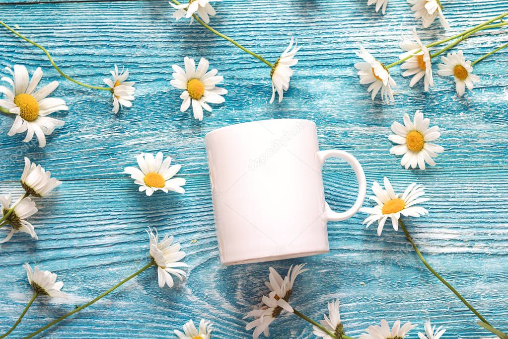 White coffee mug with chamomile flowers on blue wooden backgroun
