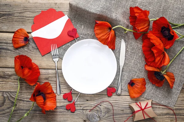 Festive table setting with red poppies, gift box and envelope on