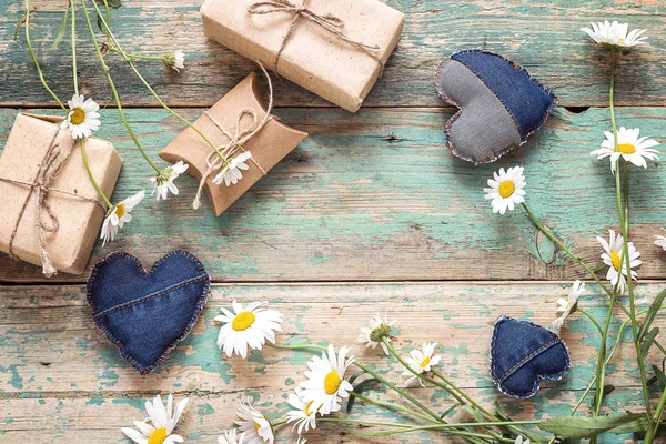 Plattelandsachtergrond met madeliefjes, decoratieve harten en geschenkverpakkingen. — Stockfoto