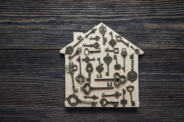 Handmade home symbol with vintage keys on wooden background.