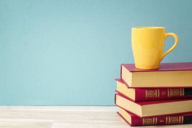 Kitaplar ve sarı kupa mavi arka plan karşı yığını. Kopya girintili
