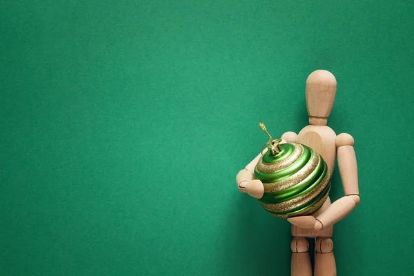 Classic wooden dummy holds Christmas ball on a green background. — Stock Photo, Image