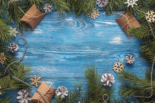 Frame from pine branches and gift boxes on blue wooden backgroun