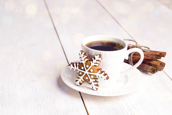 Cup of coffee with gingerbread snowflake and cinnamon sticks on