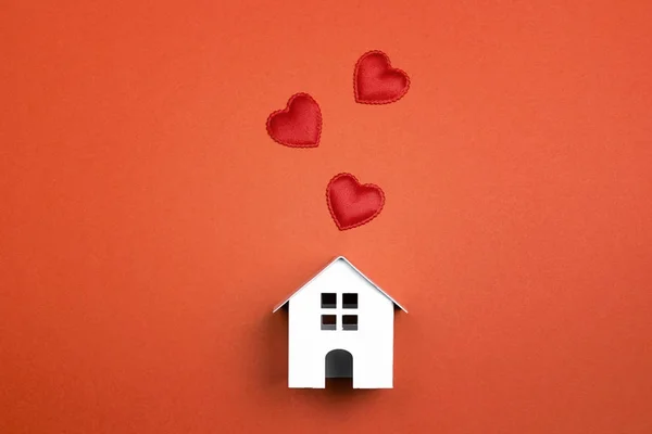 Casa de brinquedo branca em miniatura com corações no fundo vermelho . — Fotografia de Stock