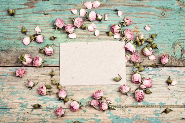 Tarjeta de papel en blanco con pequeñas rosas rosadas sobre turquesa de madera vieja — Foto de Stock