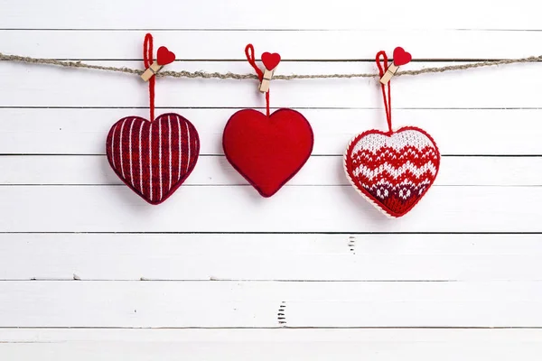 Hanging on clothespins red hearts on white wooden background. Sp