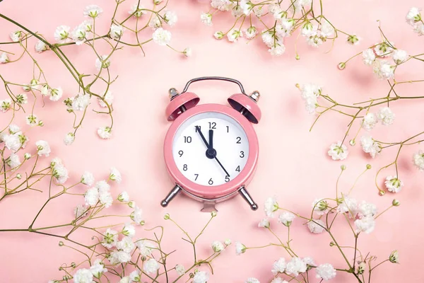 Ροζ ρολόι συναγερμών και λεπτή μικρά λευκά λουλούδια στο ροζ backg — Φωτογραφία Αρχείου