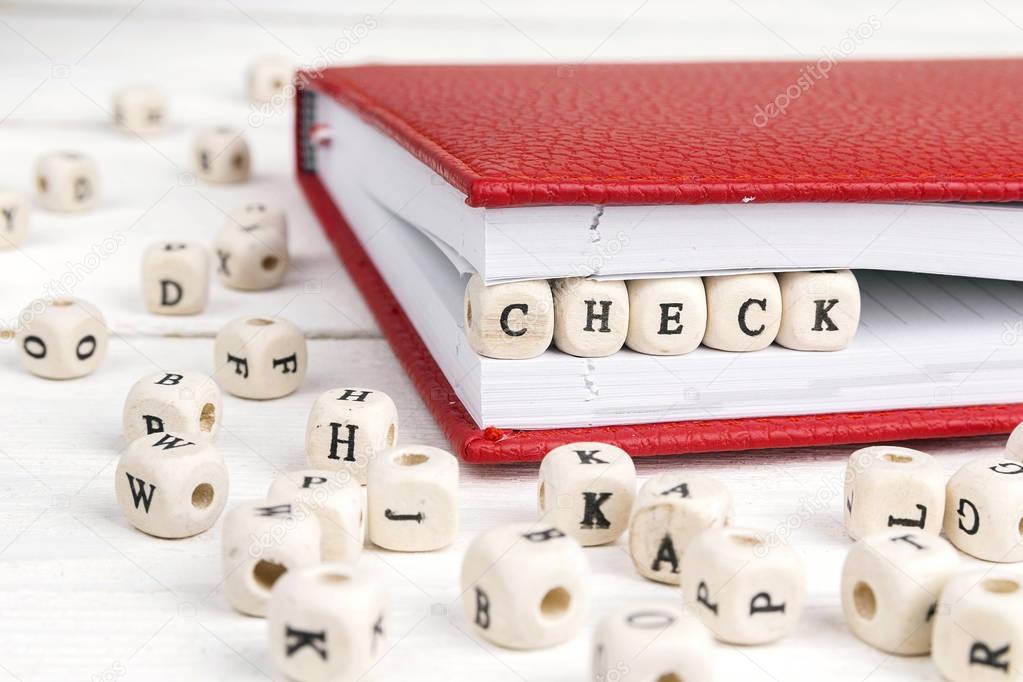 Word Check written in wooden blocks in notebook on white wooden 