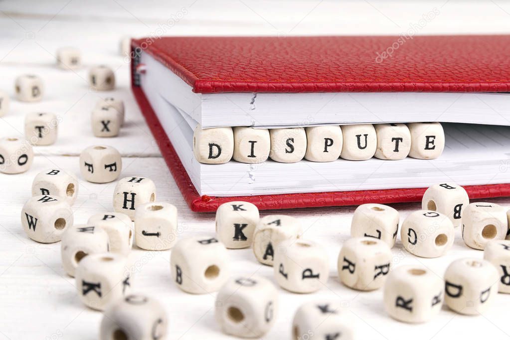 Word Dispute written in wooden blocks in red notebook on white w