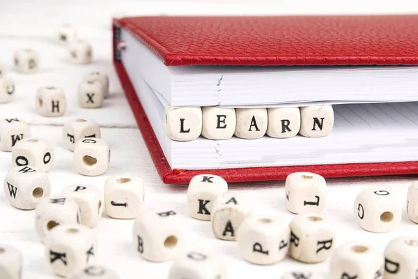 Word Learn written in wooden blocks in red notebook on white woo — Stock Photo, Image