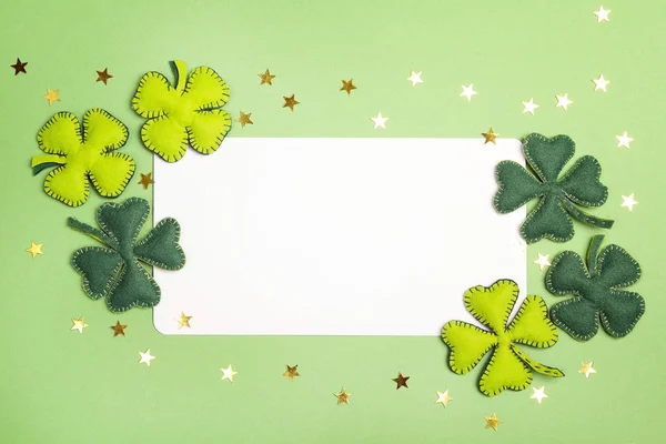 Tarjeta blanca en blanco con hojas de fieltro de trébol sobre fondo verde . —  Fotos de Stock