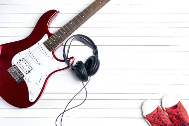 Elektro gitar ile kulaklık ve beyaz tahta üzerinde kırmızı spor ayakkabılar