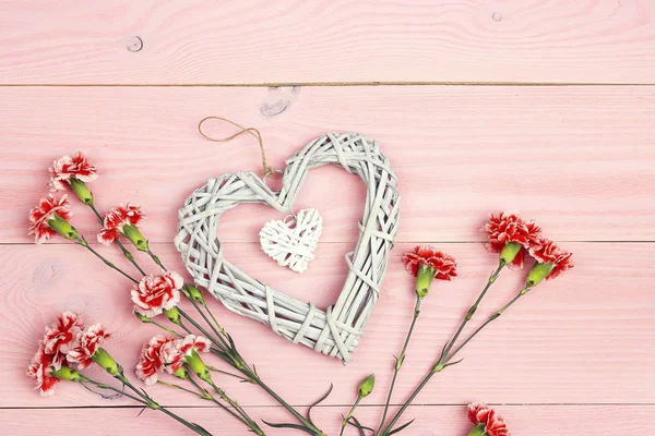 Corazón decorativo y flores de clavel sobre mesa de madera rosa . —  Fotos de Stock