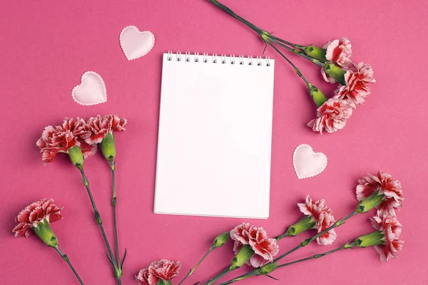 Open blank notepad with carnations flowers on a fuchsia background. Top view, place for text.