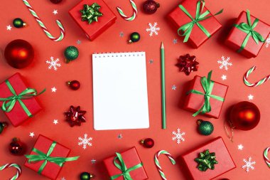 Blank notebook with Christmas composition of gifts  and decoration on a red background. Place for a wish list, gifts or goals for the year. Flat Lay, top view