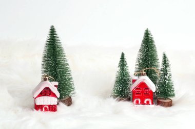 Beyaz kürk arka planında köknar ağaçları olan iki minyatür ev. Birlikte