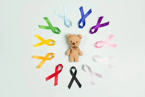 Urso de brinquedo com círculo de fitas de consciência coloridas na parte traseira azul — Fotografia de Stock