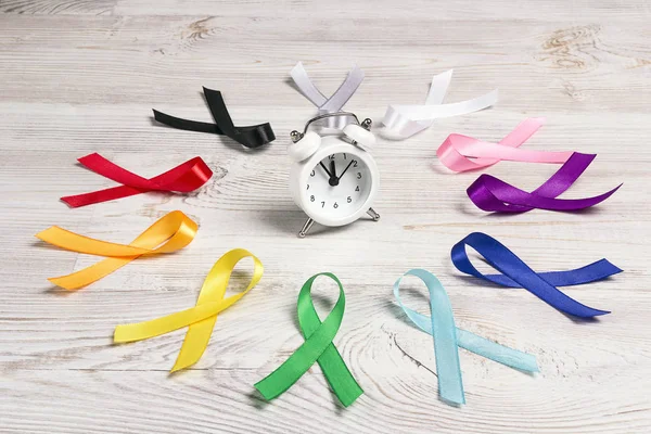 Alarm clock with colorful awareness ribbons on wooden background — 스톡 사진