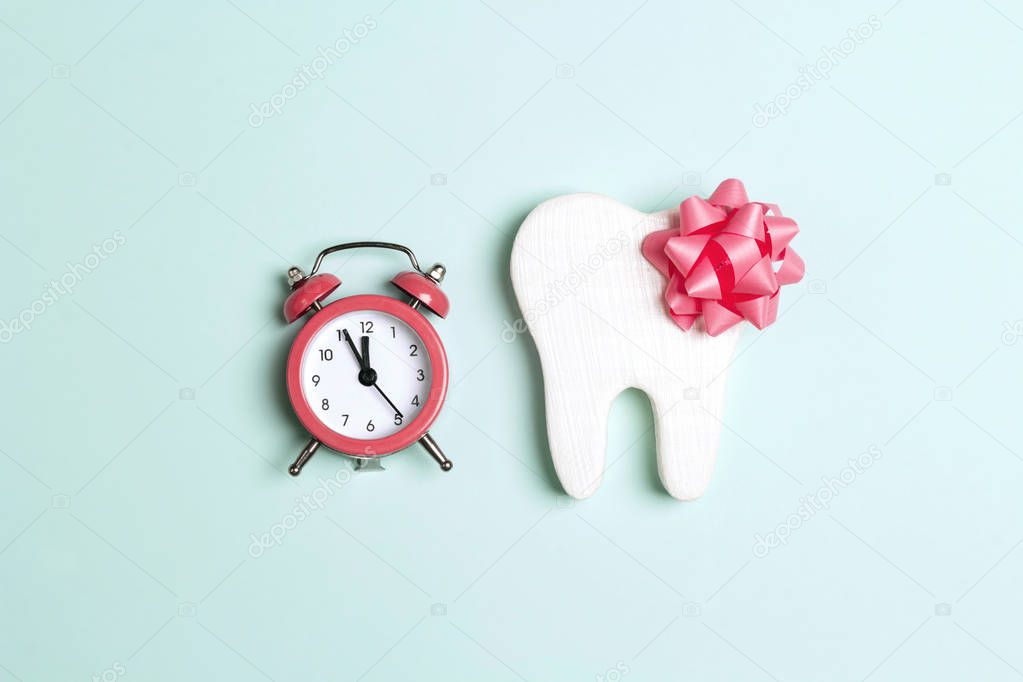 Tooth with bow and alarm clock on a blue background. 