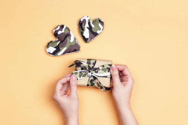 Vrouwelijke handen met een geschenkdoos met khaki lint en camouflage — Stockfoto