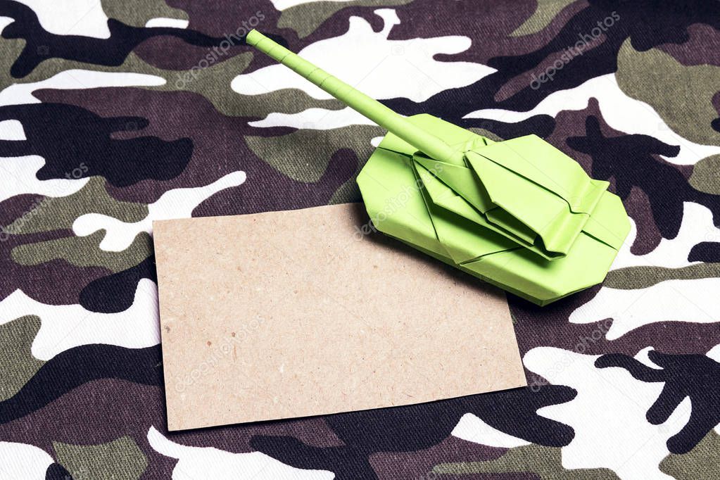 Origami paper tank with blank card on military textile backgroun
