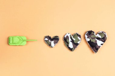 Origami kağıt tankı sarı arka planda kamuflaj kalpleri fırlatır