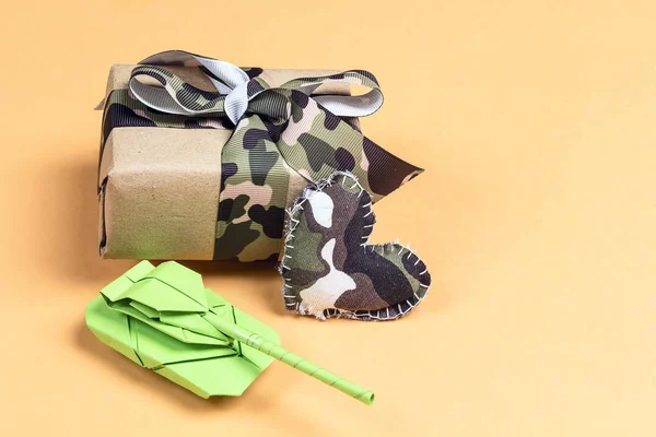 Gift box with camouflage ribbon, paper tank and khaki hearts on — Stock Photo, Image