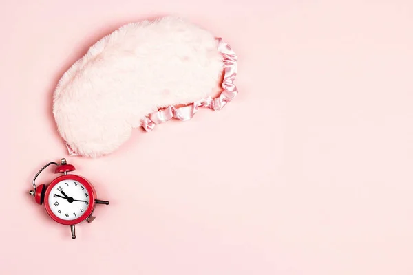 ふわふわの睡眠アイマスクとピンクの背景に目覚まし時計 テキストのスペースをコピーします 健康的な睡眠 不眠症 旅行の概念 — ストック写真