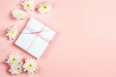 Pembe arka planda kasımpatı çiçekleri olan hediye kutusu. Boşluğu kopyala, üst görünüm.