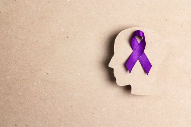 Kahverengi karton arka planda mor farkındalık kurdelesi ve baş silueti. Epilepsi hastalığı ya da Alzheimer Hastalığı Dünya Farkındalığı Günü.