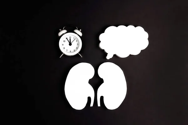 White human kidney symbol with empty speech bubble and alarm clock on black background. World Kidney Day. Kidney health concept. Flat lay, top view.