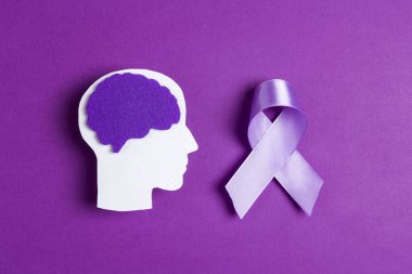 Mor farkındalık kurdelesi ve menekşe arkaplanda beyin sembolü. Epilepsi hastalığı ya da Alzheimer Hastalığı Dünya Farkındalığı Günü.