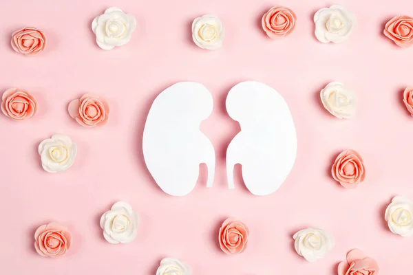 Human kidney symbol surrounded by flowers on pink background. World Kidney Day. Kidney health concept. Flat lay, top view.