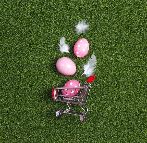 Shopping trolley with Easter eggs on a green grass background. Easter shopping and sale.