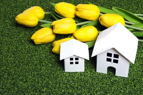 Two white model house on green decorative lawn with bouquet of yellow tulips. Ecology housing, eco home. Mortgage, construction and property investment.