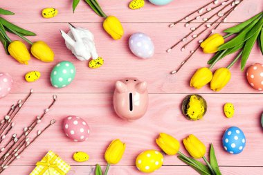 Yumurtalarla çevrili domuz kumbarası ve pembe ahşap arka planda Paskalya süslemeleri. Paskalya tatili için para biriktiriyorum..